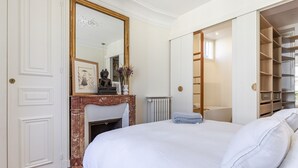 A bedroom with a large bed, a fireplace, a wardrobe, and a mirror. - Appartement Haussmannien D'exception Coeur de Paris (Paris)