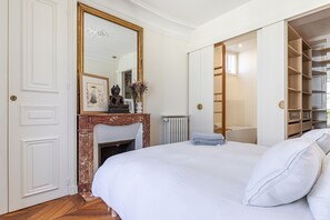 A bedroom with a large bed, a fireplace, a wardrobe, and a mirror. - Appartement Haussmannien D'exception Coeur de Paris (Paris)