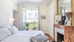 A hotel room with a large bed, a fireplace, and a balcony with a view of buildings. - Appartement Haussmannien D'exception Coeur de Paris (Paris)
