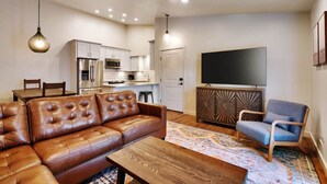 A modern living room with a brown leather sofa, a wooden coffee table, a blue armchair, and a flat-screen TV.
