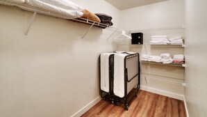A compact room with a bed, a suitcase, and shelves with folded towels.
