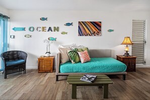 Ein Zimmer mit einem Bett, einem Sessel, einem Tisch und Wanddekorationen, darunter Fische und das Wort „OCEAN“.