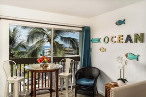 Ein Balkon mit Blick auf Palmen und das Meer, ein runder Tisch mit Stühlen und dekorative Fische an der Wand.