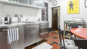 A modern kitchen with stainless steel appliances, a sink, and a dining area with a red table and black chairs.