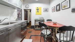 A compact kitchen with stainless steel appliances, a dining area with a red table and black chairs, and a wall clock.