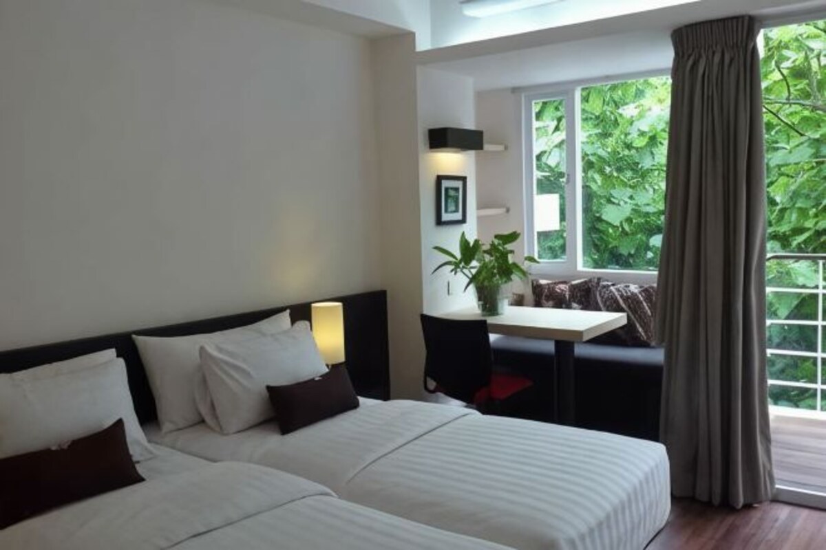 Une chambre d’hôtel avec deux lits, une petite table avec une plante, une fenêtre avec des rideaux et une vue sur la verdure à l’extérieur.