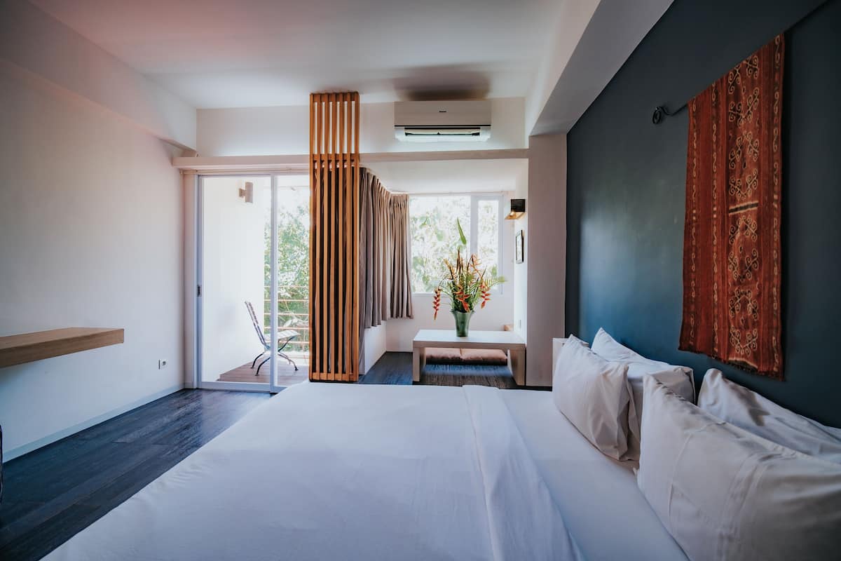 Una camera d'albergo moderna con un grande letto, un'area salotto con un vaso di fiori e vista sull'esterno.