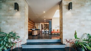 A modern interior with a staircase leading to a dining area, featuring a wooden wall, potted plants, and a central island with seating. - Allia Residence Nusa Dua (Nusa Dua)