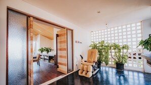 A modern interior with a massage chair, potted plants, and a wooden-framed sliding door leading to another room. - Allia Residence Nusa Dua (Nusa Dua)