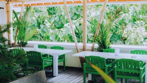 An outdoor patio area with white tables and green chairs, surrounded by lush greenery and a bamboo pergola. - Allia Residence Nusa Dua (Nusa Dua)