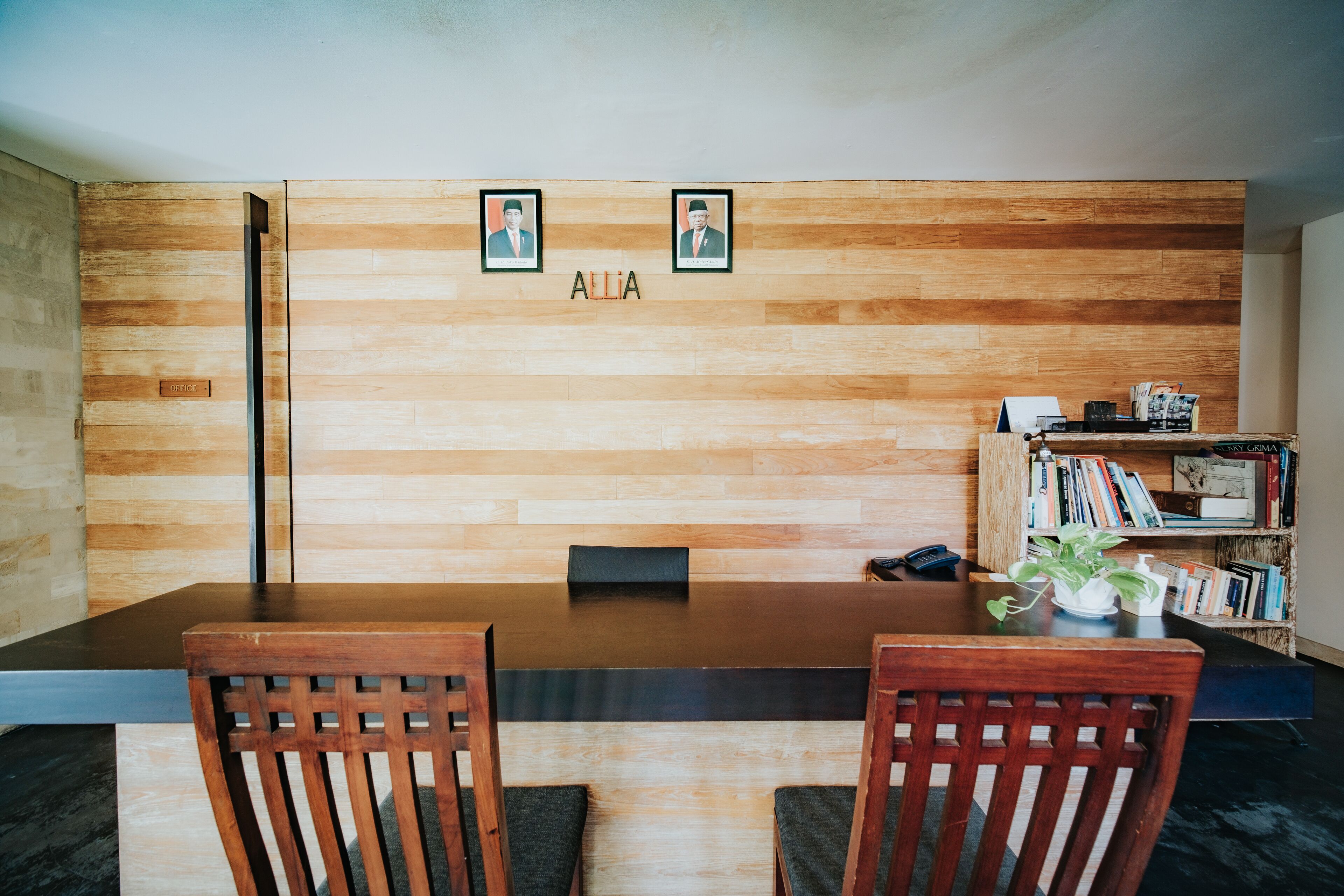 A conference room with a wooden wall, two framed photos, and the name "ALLIA" above the wall.