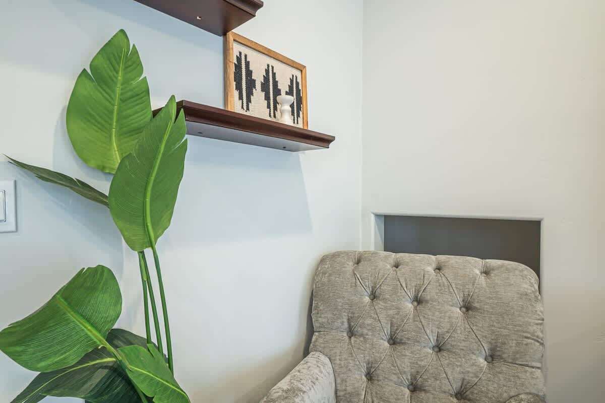 Una habitación con un sillón tapizado, una planta verde grande y un cuadro en la pared.