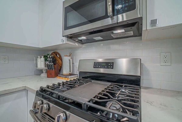 A modern kitchen with stainless steel appliances, including a stove and microwave, and white tiled walls.