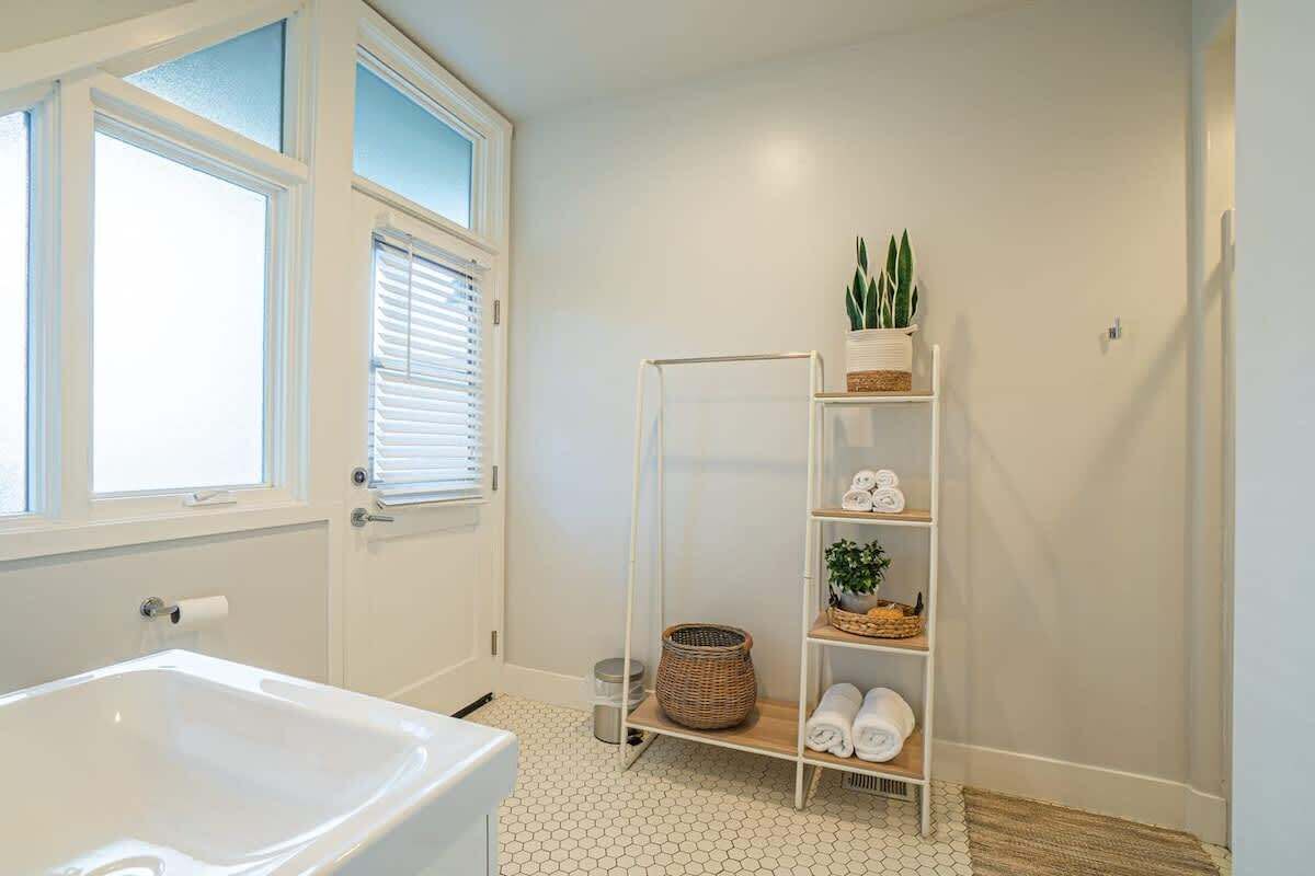 A bathroom with a white bathtub, a white shelf with towels and a plant, and a hexagonal tiled floor.