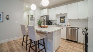 Una cocina moderna con armarios blancos, una isla central con taburetes de bar, lavavajillas y refrigerador.