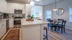 A modern kitchen with white cabinets, a central island, stainless steel appliances, and a dining area with dark wooden chairs and a round table.