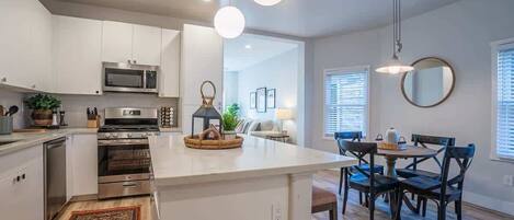 A modern kitchen with white cabinets, a central island, stainless steel appliances, and a dining area with dark wooden chairs and a round table.