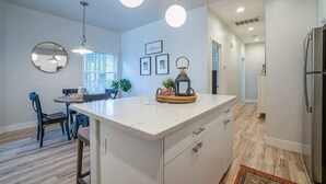 A modern kitchen with a central island, pendant lights, and a dining area with a table and chairs.