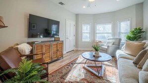 A spacious living room with a ceiling fan, a flat-screen TV, a sofa, a coffee table, and a decorative rug.