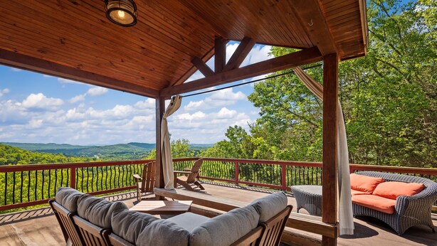 Una terraza de madera con mobiliario exterior, una pérgola y una vista panorámica de un viñedo y montañas.
