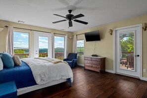 A bedroom with a bed, a chair, a dresser, and a TV. There are windows and a door. - 4Bdr Secluded! Hot Tub, Pool Table, & Spectacular Views. (Holiday Island)