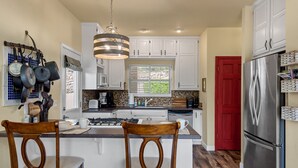Una cocina con armarios blancos, un refrigerador de acero inoxidable, una puerta roja y un colgador para ollas.
