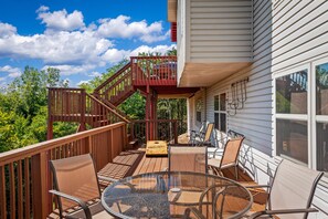 A deck with a glass table and chairs, a wooden staircase, and a view of trees and sky. - 4Bdr Secluded! Hot Tub, Pool Table, & Spectacular Views. (Holiday Island)