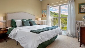 Un dormitorio con una cama grande, una mesita de noche, un aparador, una ventana con cortinas y vistas al exterior.