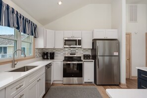 A modern kitchen with white cabinets, stainless steel appliances, a built-in microwave, a refrigerator, and a coffee maker.
