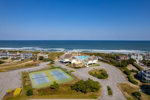 A coastal residential area with houses, a tennis court, and a view of the ocean.