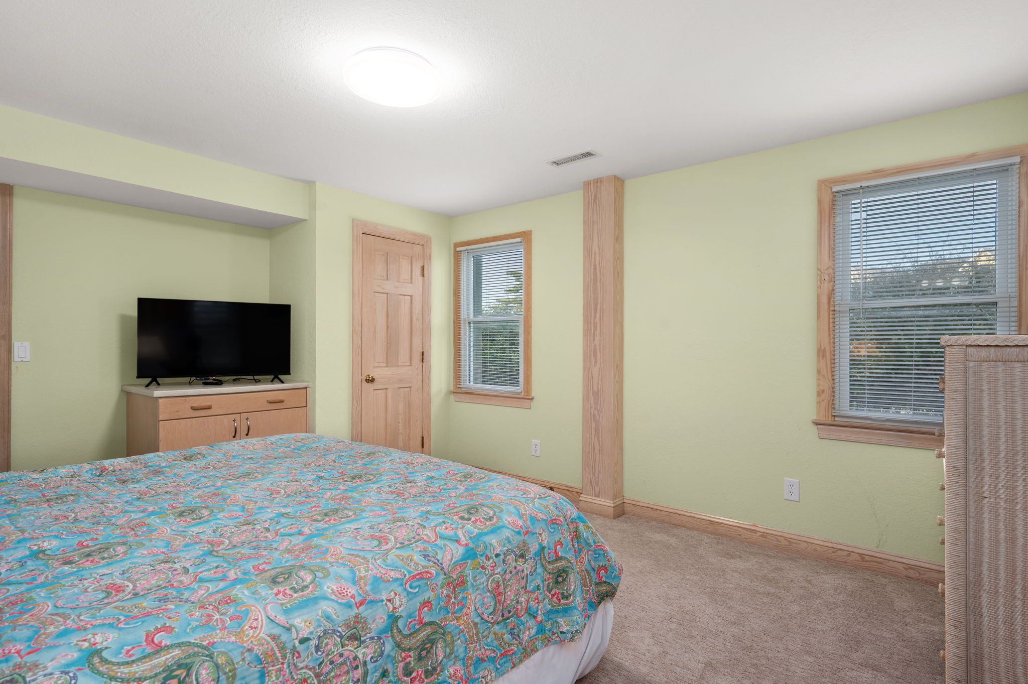 A bedroom with a bed, a television on a dresser, a window with blinds, and a door.