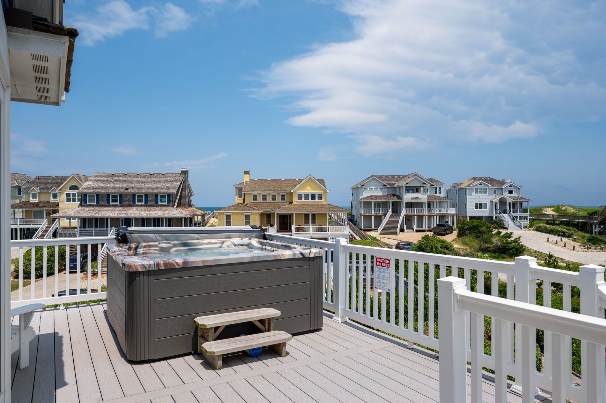 A deck with a hot tub, wooden benches, and a white fence overlooking beach houses.