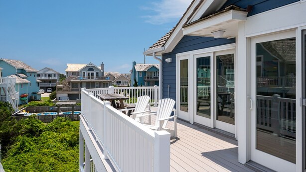 A residential deck with white railings and chairs, overlooking a pool and neighboring houses. - C-Side: Semi-oceanfront, hot tub, community oceanfront pool, walkway to beach by house. (Nags Head)