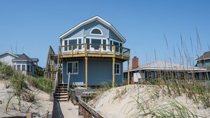 A two-story beach house with a balcony, wooden deck, and a sandy beach in the background. - SeaAira: Oceanfront with unbeatable ocean views, renovated kitchen and baths (Nags Head)