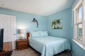 A bedroom with a bed, a nightstand, a lamp, a painting of a bird, and a window.