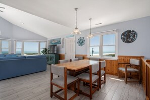 A spacious living area with a wooden dining table, blue sofa, and large windows overlooking the beach.