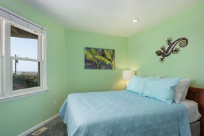 A bedroom with a bed, a window, a painting, and a wall-mounted light fixture.