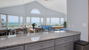 A spacious kitchen with large windows overlooking the ocean, a ceiling fan, and a view of the beach. - SeaAira: Oceanfront with unbeatable ocean views, renovated kitchen and baths (Nags Head)