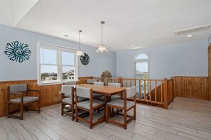 A dining area with a wooden table and chairs, a hanging light fixture, and a view of the outside through a window.