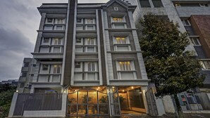 A multi-story building with a modern architectural design, featuring a central vertical element and multiple balconies. - Worldtree Suites Manyata (Bengaluru)