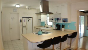 Una cocina con una isla central, taburetes de bar, una campana extractora de acero inoxidable y un refrigerador.
