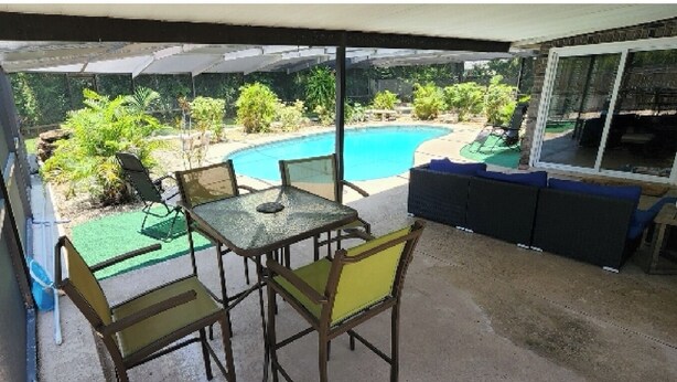 Un patio cubierto con piscina, mobiliario exterior y una mesa con sillas.