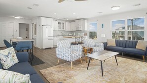 A modern living room with a sofa, chairs, a coffee table, and a kitchen area with white cabinets and appliances. - The Regal Beagle: 2  BR, 2  BA House in Crystal Beach, Sleeps 8 (Bolivar Peninsula)