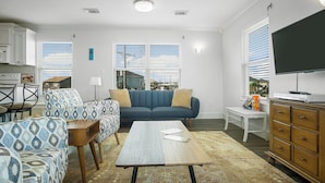 A living room with a sofa, chairs, a coffee table, a TV, and a kitchen area with a stove. - The Regal Beagle: 2  BR, 2  BA House in Crystal Beach, Sleeps 8 (Bolivar Peninsula)