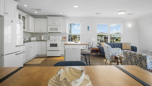 A modern kitchen with white cabinets, a microwave, and a stove. There is a dining area with a wooden table and chairs. - The Regal Beagle: 2  BR, 2  BA House in Crystal Beach, Sleeps 8 (Bolivar Peninsula)