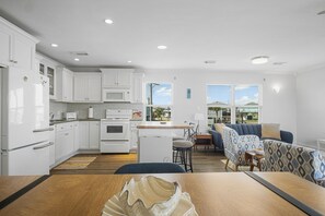 Una cocina moderna con armarios blancos, un microondas y una estufa. Hay una zona de comedor con una mesa y sillas de madera.