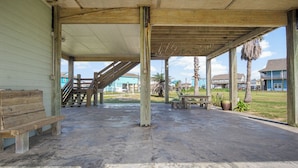 A covered outdoor area with a concrete floor, wooden benches, and a staircase leading to an upper level. - The Regal Beagle: 2  BR, 2  BA House in Crystal Beach, Sleeps 8 (Bolivar Peninsula)