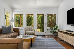 Ein modernes Wohnzimmer mit einem braunen Ledersofa, einem runden Couchtisch, einem beigen Sessel und einer großen Pflanze in einem Topf.