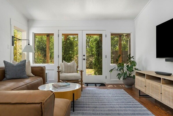 Ein modernes Wohnzimmer mit einem braunen Ledersofa, einem runden Couchtisch, einem beigen Sessel und einer großen Pflanze in einem Topf.