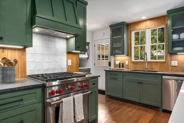Cocina con armarios verdes, estufa de acero inoxidable y lavavajillas.